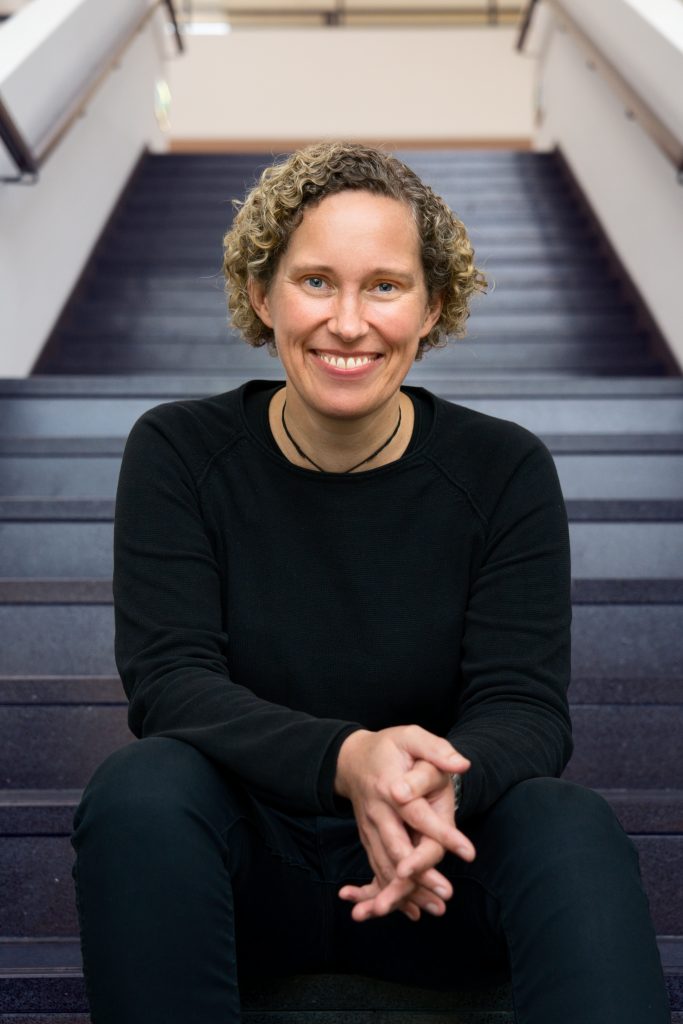 Hille Gerdes, Coach für mentale Gesundheit und Stressbewältigung, lächelnd auf einer Treppe.
